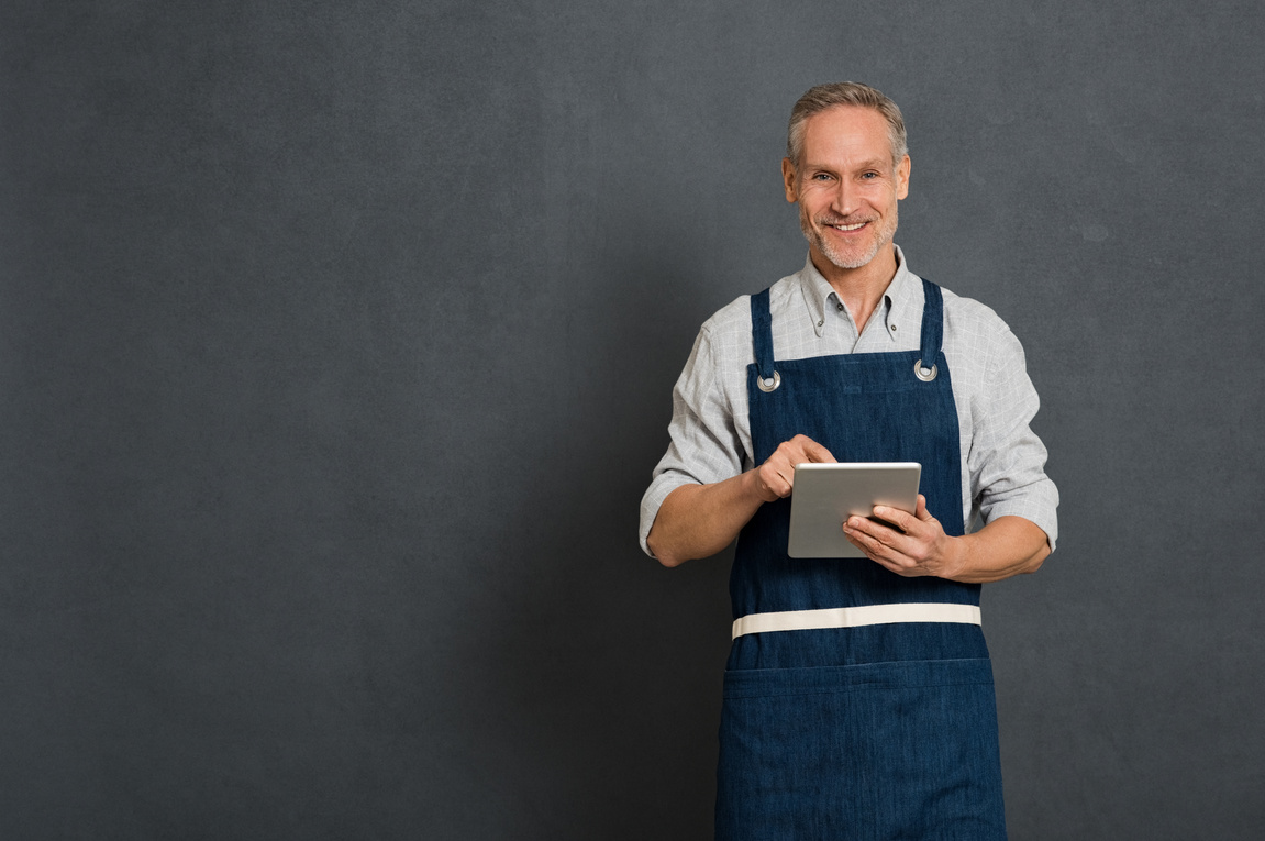 A small business owner in an apron using a tablet computer for his digital marketing