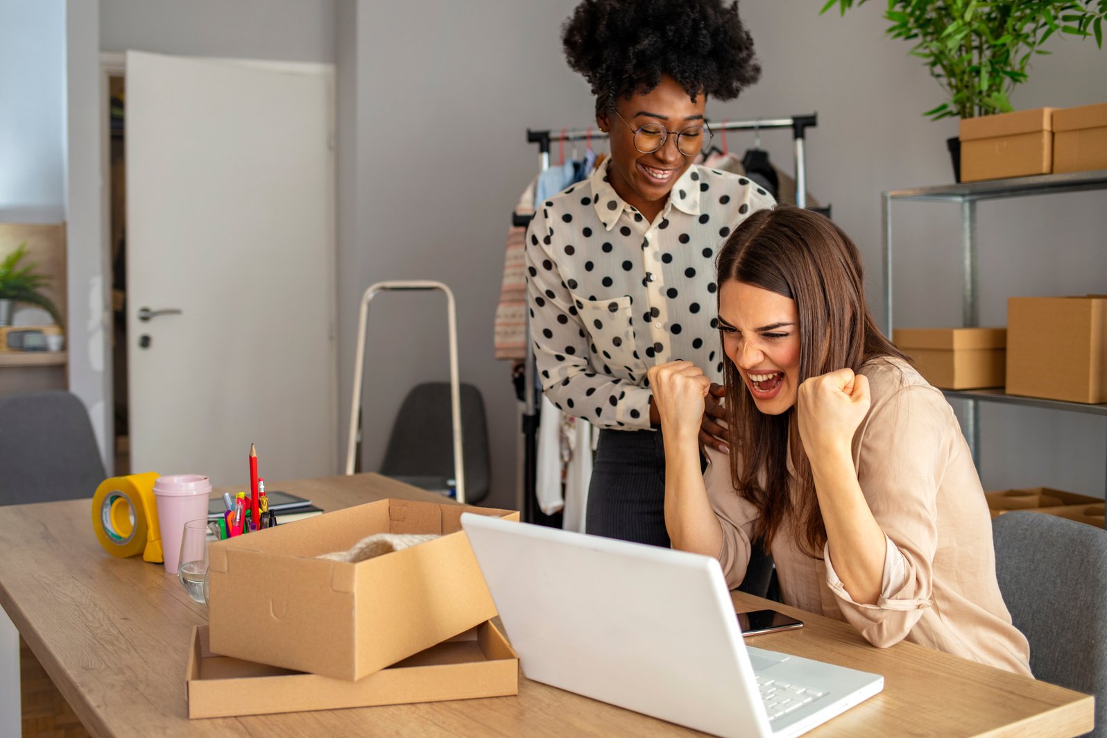 Two small business owners in an office celebrating their digital marketing strategy at a laptop